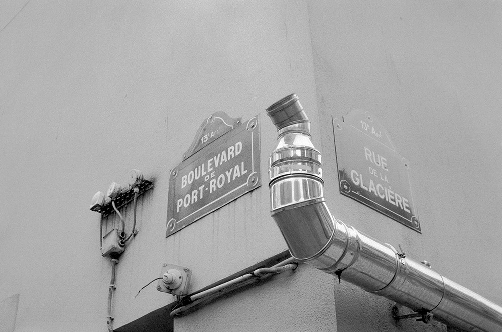 horizontal black and white photo of two street signs and a metal pipe on the corner of a wall